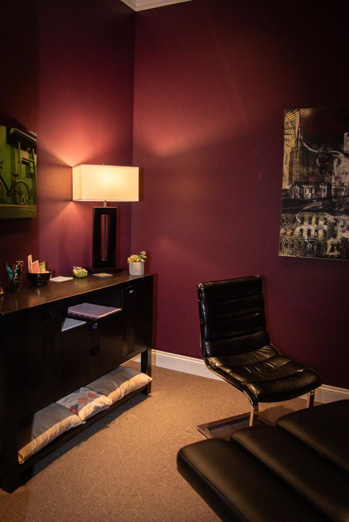 A treatment room in deep plum, lit by a table lamp